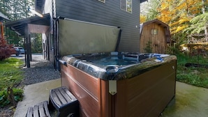 Un jacuzzi dans un jardin, avec une maison et un abri en bois en arrière-plan.