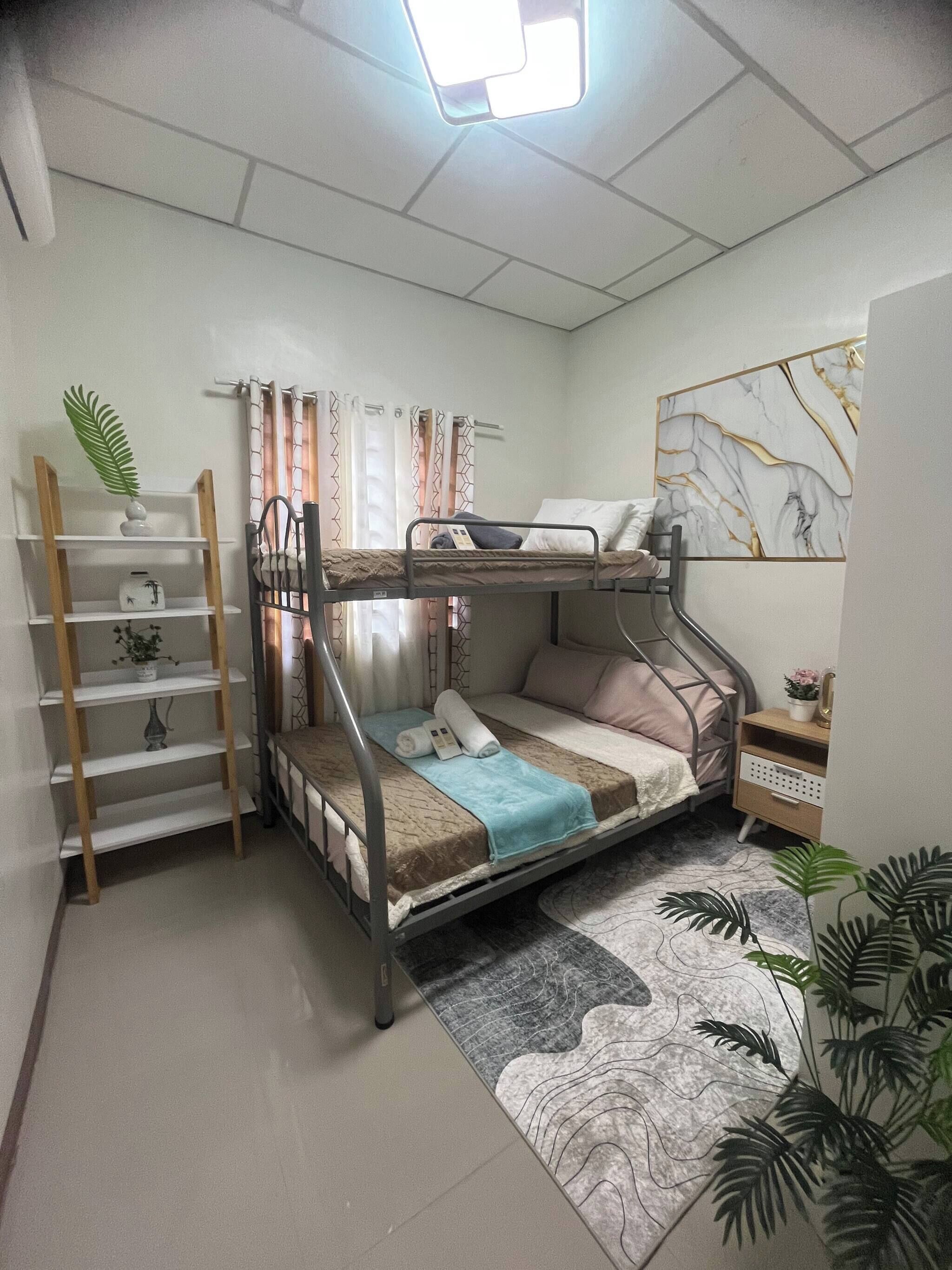 Habitación con literas, una escalera de madera, una mesita de noche pequeña, estante en la pared y una alfombra estampada.