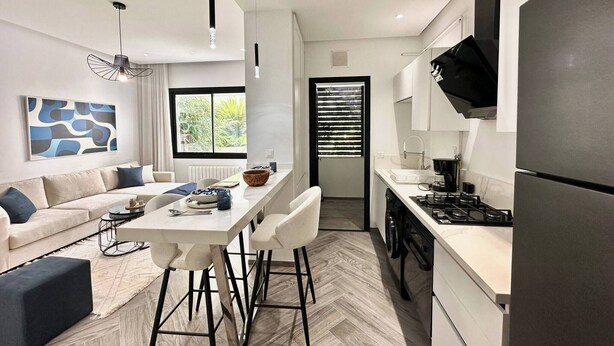A modern kitchen with a built-in stove, a refrigerator, and a dining area with a white table and chairs. - Topaz - Bright Apartment Lake 2 (Tunis)