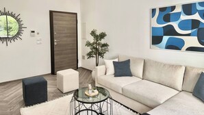 A modern living room with a sofa, a glass coffee table, a decorative mirror, a door, and a wall art piece. - Topaz - Bright Apartment Lake 2 (Tunis)