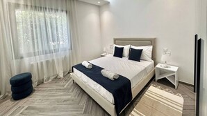 A modern hotel room with a large bed, a bedside table with a lamp, and a view of greenery through sheer curtains. - Topaz - Bright Apartment Lake 2 (Tunis)