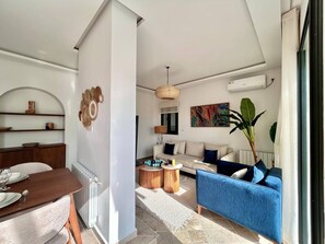 A modern living room with a sofa, a dining table set, and a large plant. - Sunny Andalouse S2 apartment in Sidi Bou Saïd (sidi bou said)