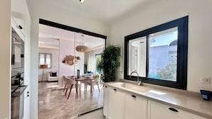Una cucina moderna con mobili bianchi, un'ampia finestra e un'area pranzo con tavolo e sedie.