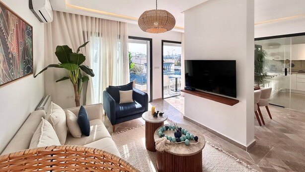 Un soggiorno moderno con un divano, una poltrona blu, una TV e un'ampia finestra.