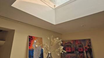 A room with a skylight, two paintings, and a vase with flowers.