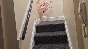 A staircase with a handrail, a sign that reads "OUR happy PLACE", and a vase with pink flowers. - Glams one bedroom apartment (West Midlands)