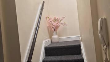 A staircase with a handrail, a sign that reads "OUR happy PLACE", and a vase with pink flowers.