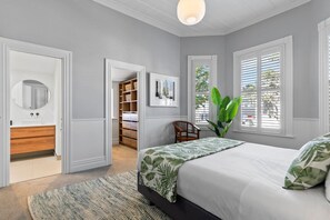 Ein Schlafzimmer mit Bett, Nachttisch, Sessel, großem Fenster und Kleiderschrank.