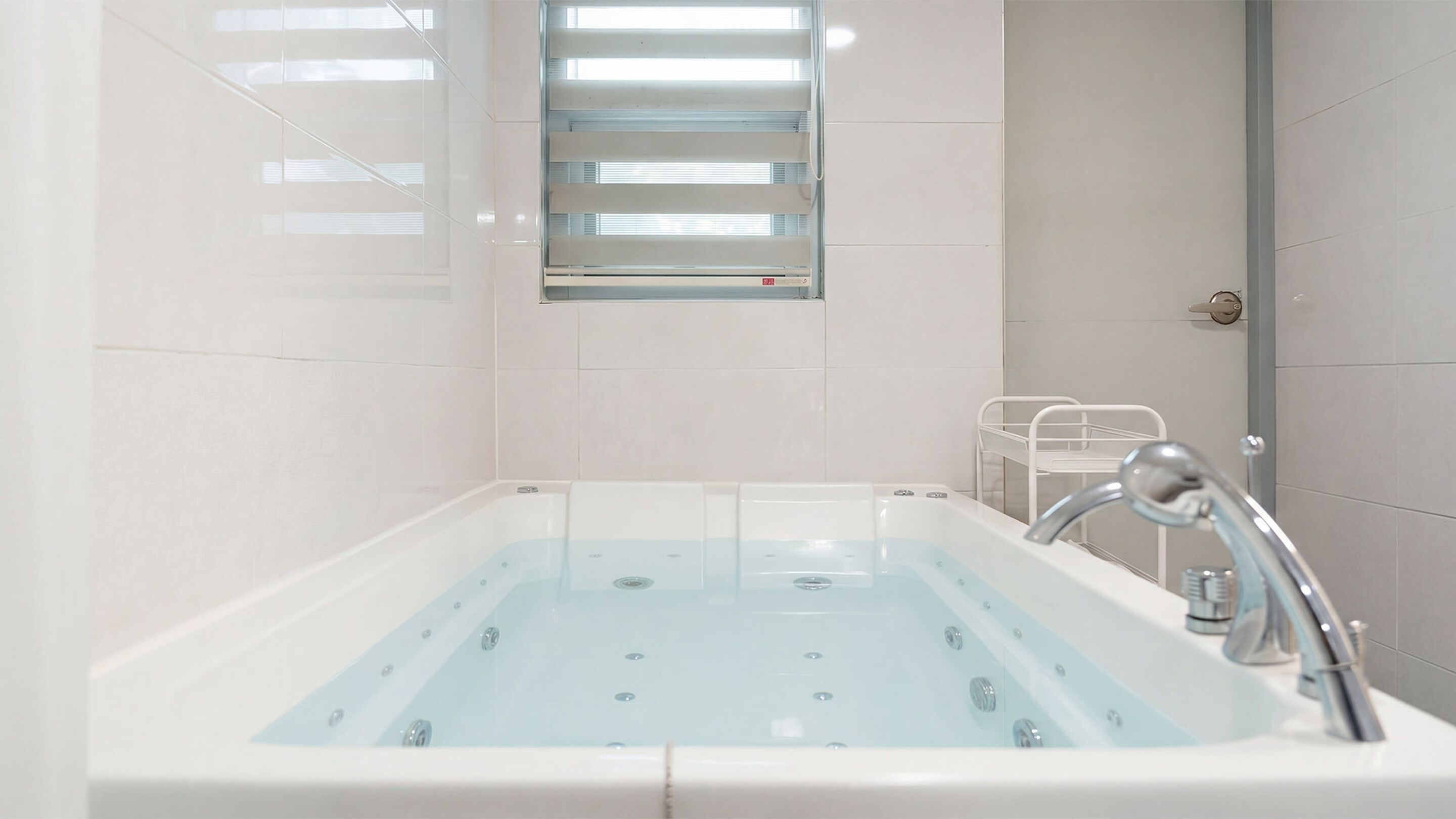 Une salle de bain moderne dotée d’une grande baignoire, d’un espace douche et d’une petite fenêtre avec des stores.