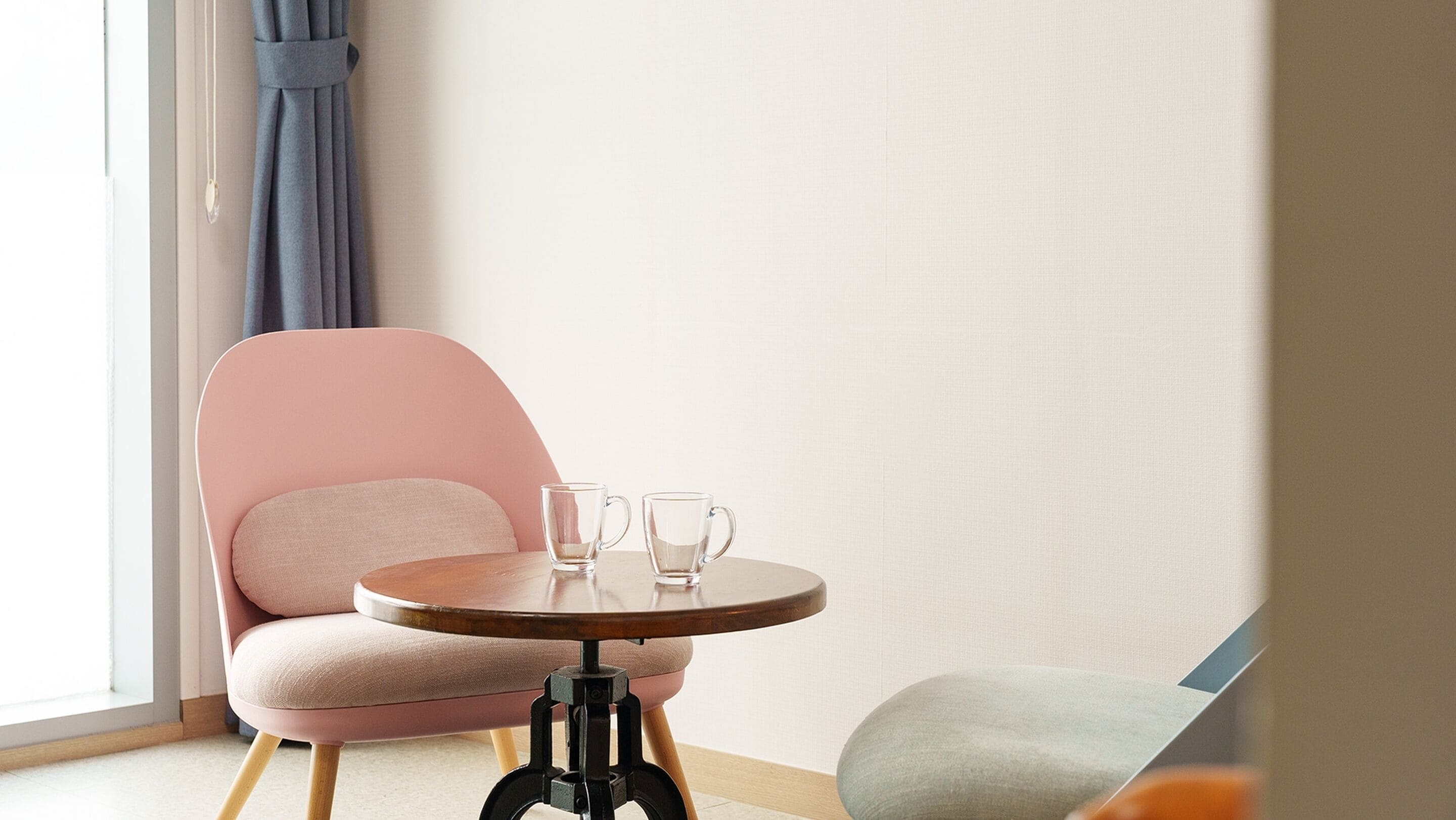 A modern room with a pink chair, a small round table, and two clear glasses.