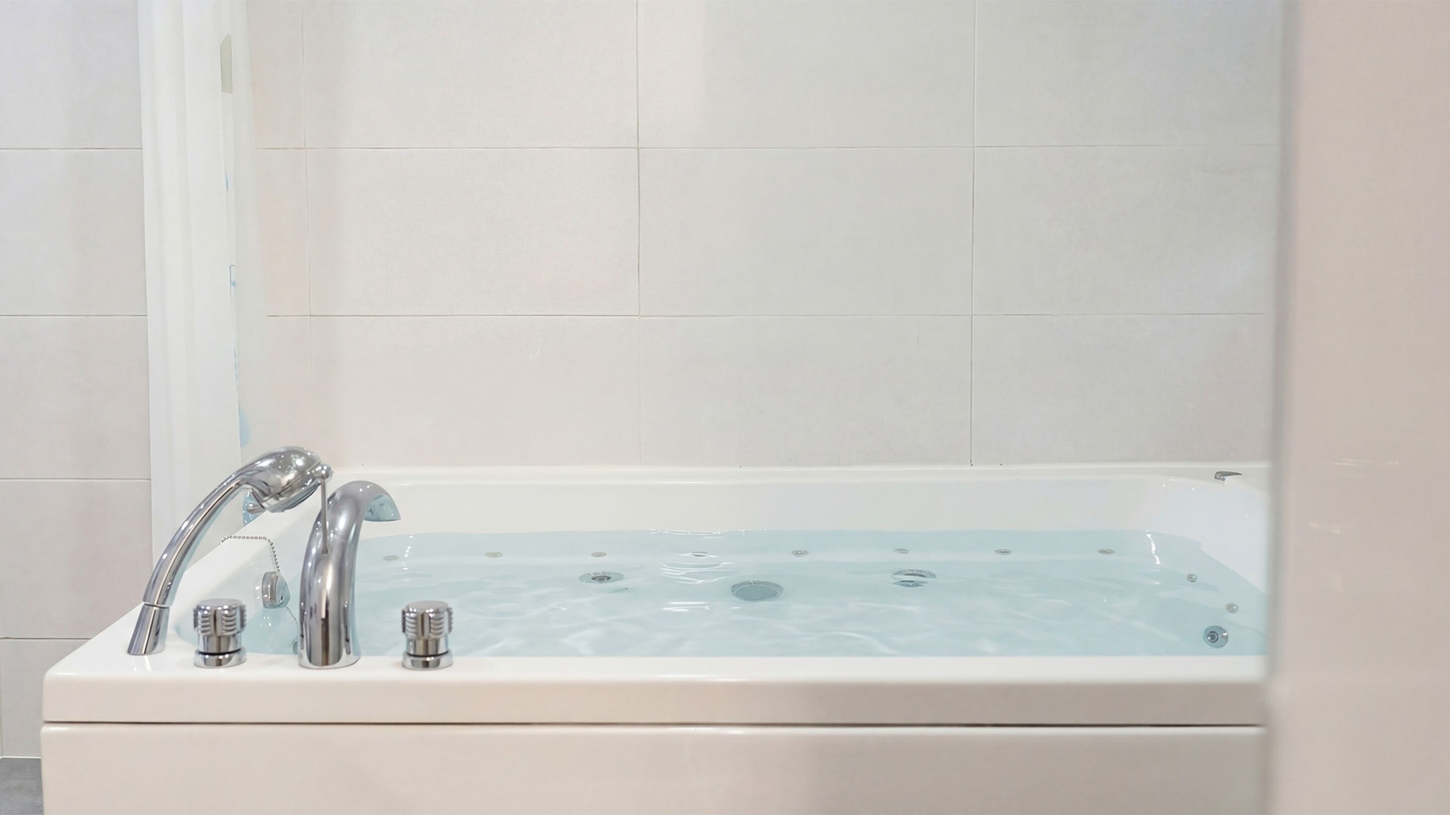 A modern bathroom with a white bathtub, chrome fixtures, and a tiled wall.