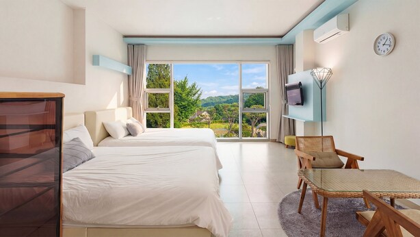 Een hotelkamer met twee bedden, een televisie, een stoel en uitzicht op de omgeving.
