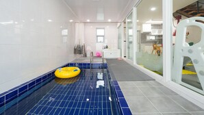 Een moderne badkamer met een blauw betegeld zwembad, een gele opblaasring en een douchecabine van glas.