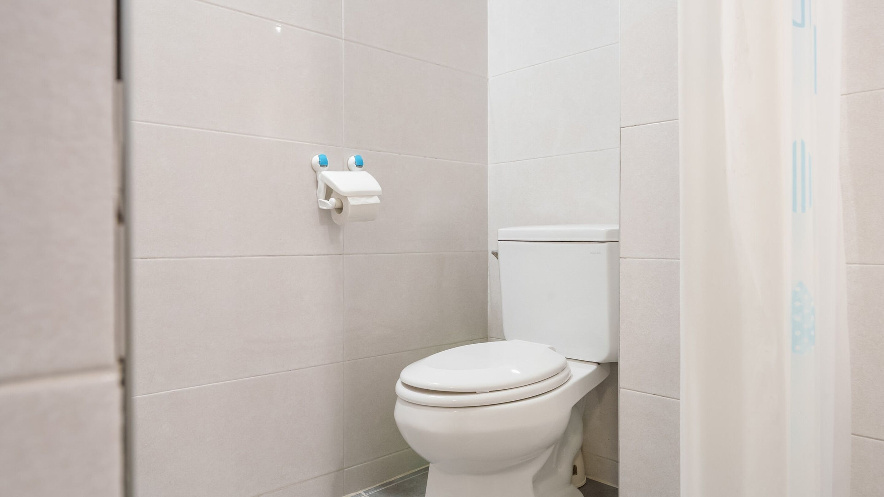 A modern bathroom with a toilet, white tiles, and a paper towel dispenser.