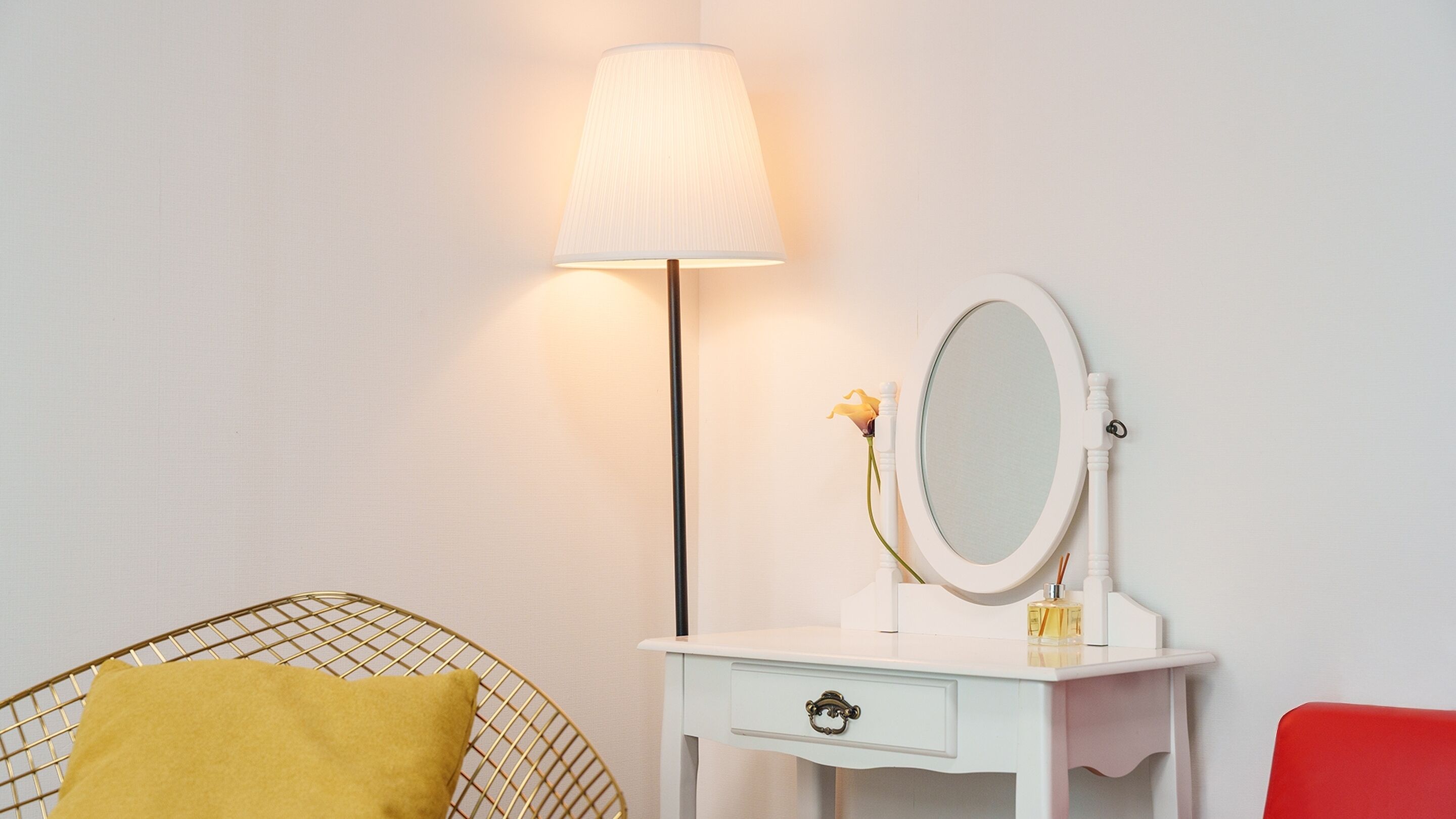 A white vanity with a mirror, a lamp, and a small vase with a flower.