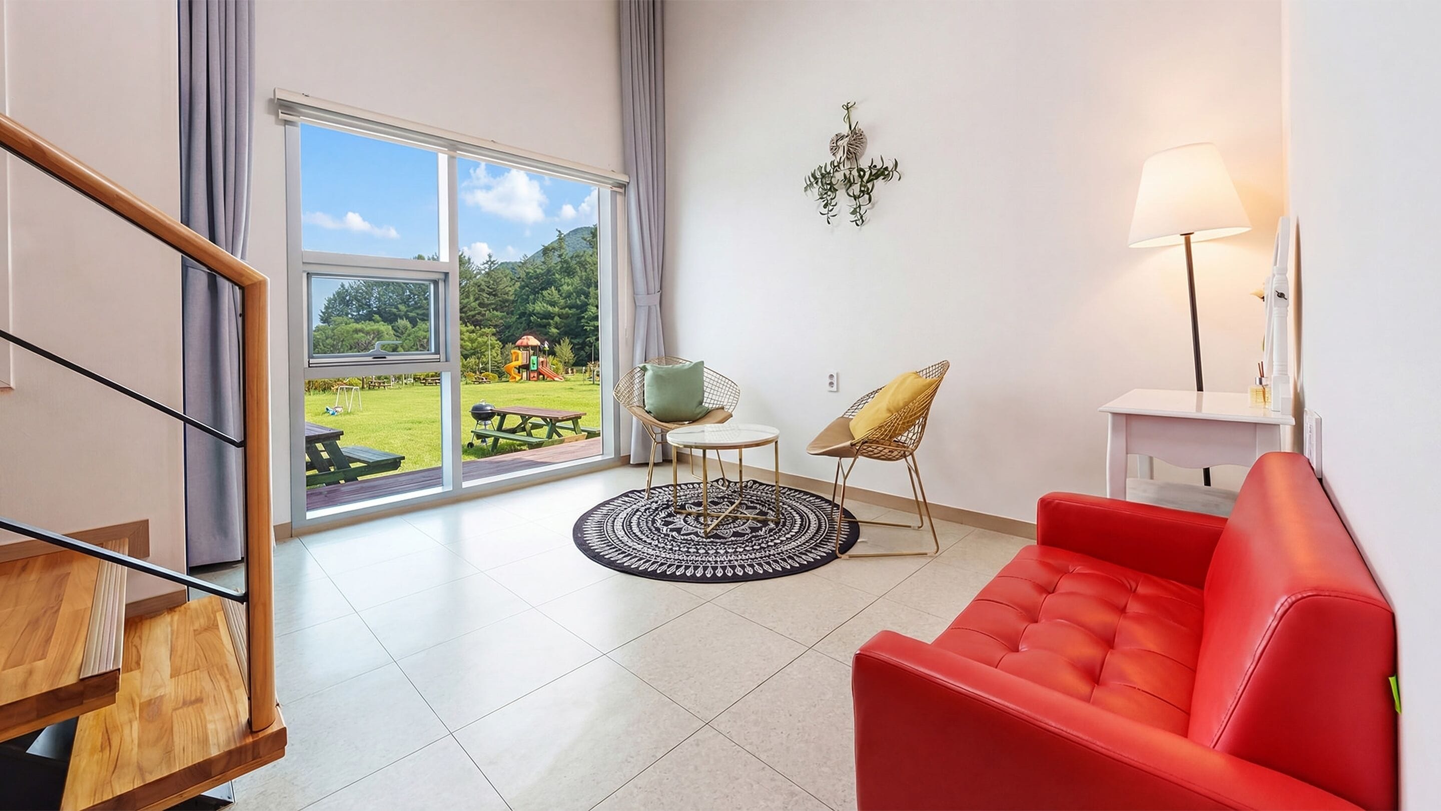 A modern living room with a red sofa, a round coffee table, and a view of a garden through large sliding glass doors.
