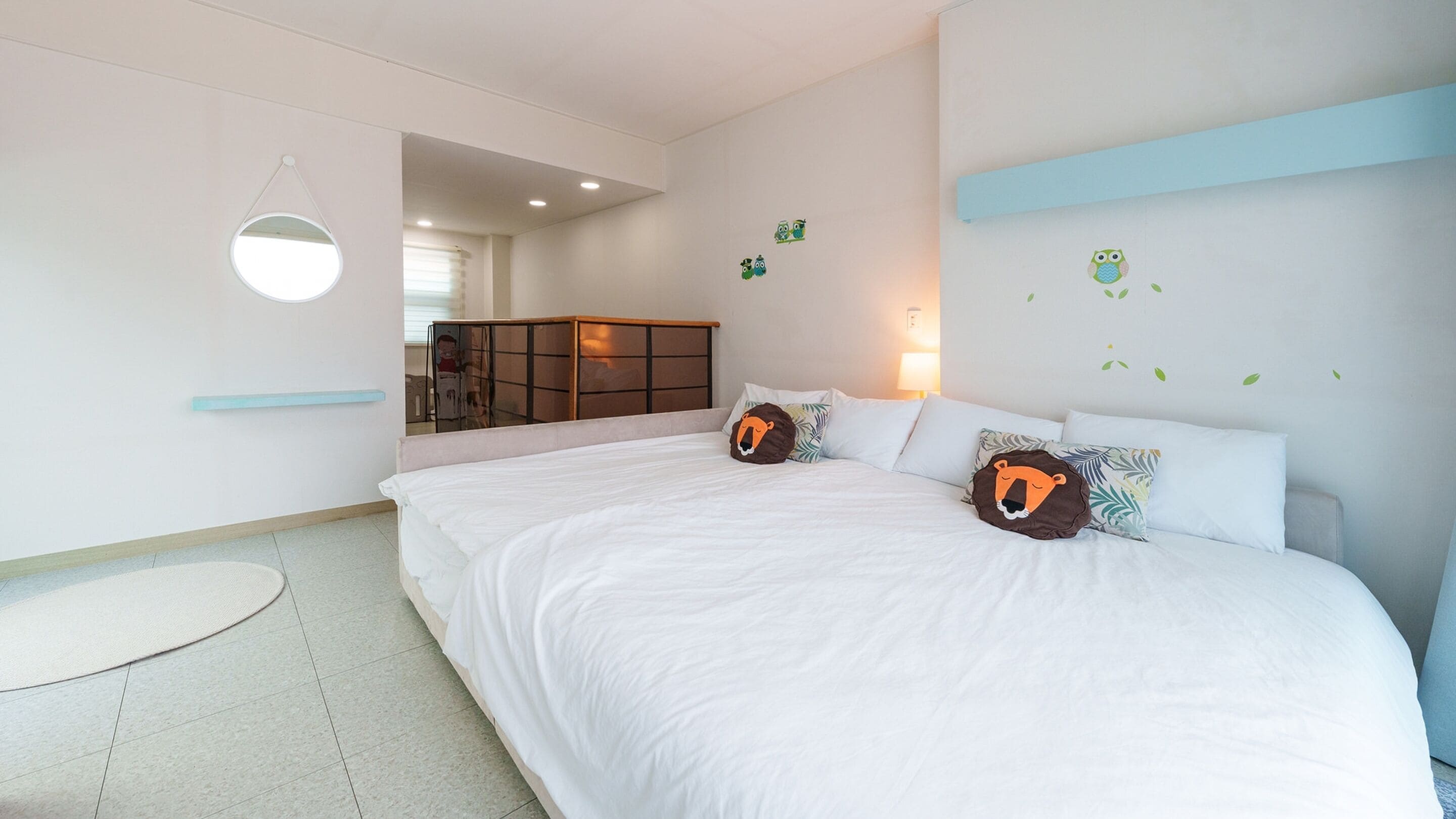 A bedroom with a large bed, two pillows with animal faces, a bedside table, and a wall-mounted light fixture.