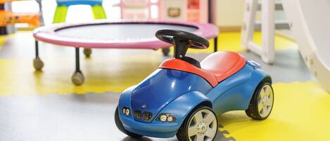 A toy car on a play mat with a trampoline and a small table in the background.