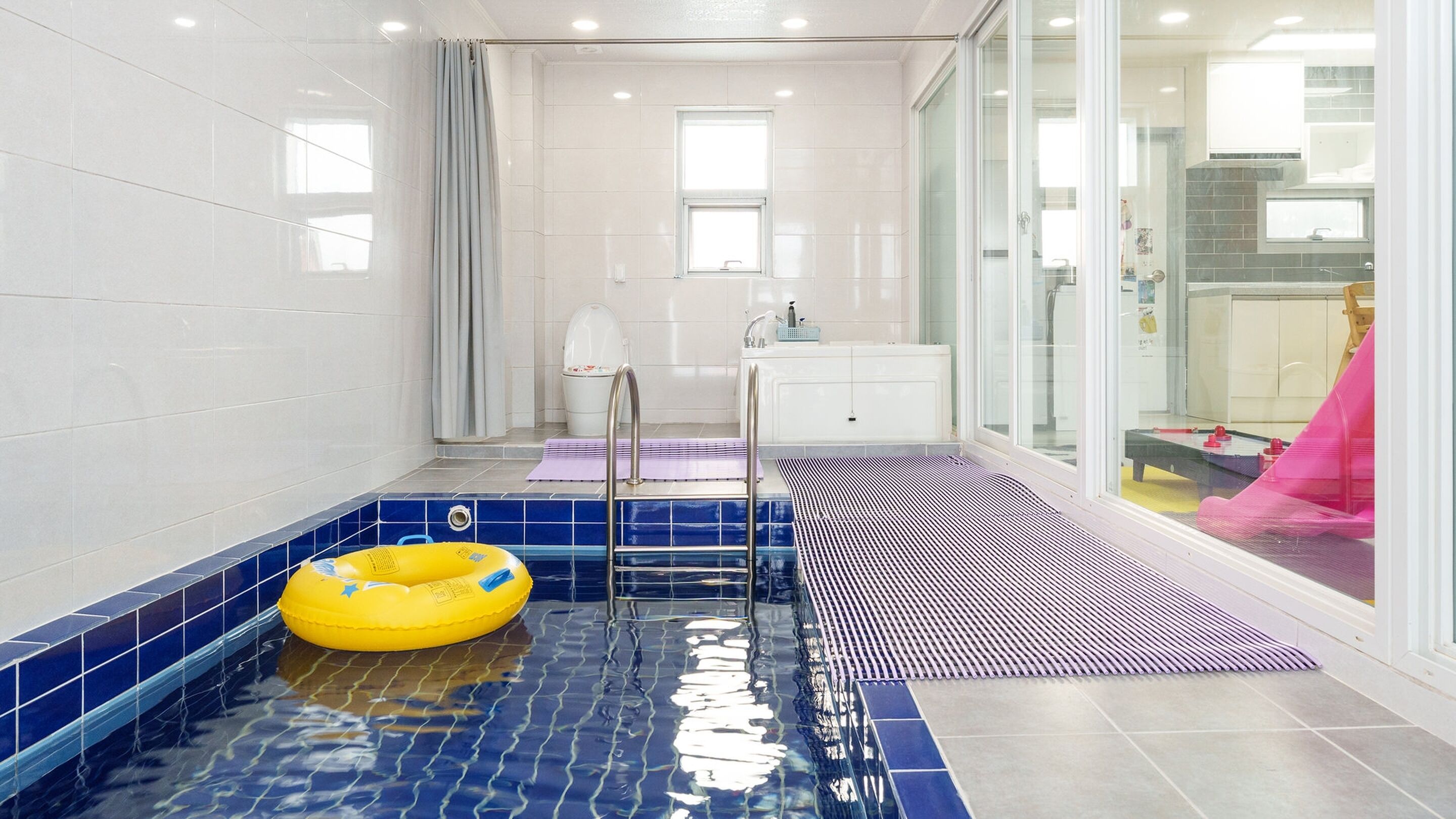 Un baño moderno con cabina de ducha de vidrio, bañera y una peque ña zona de piscina con un flotador amarillo.