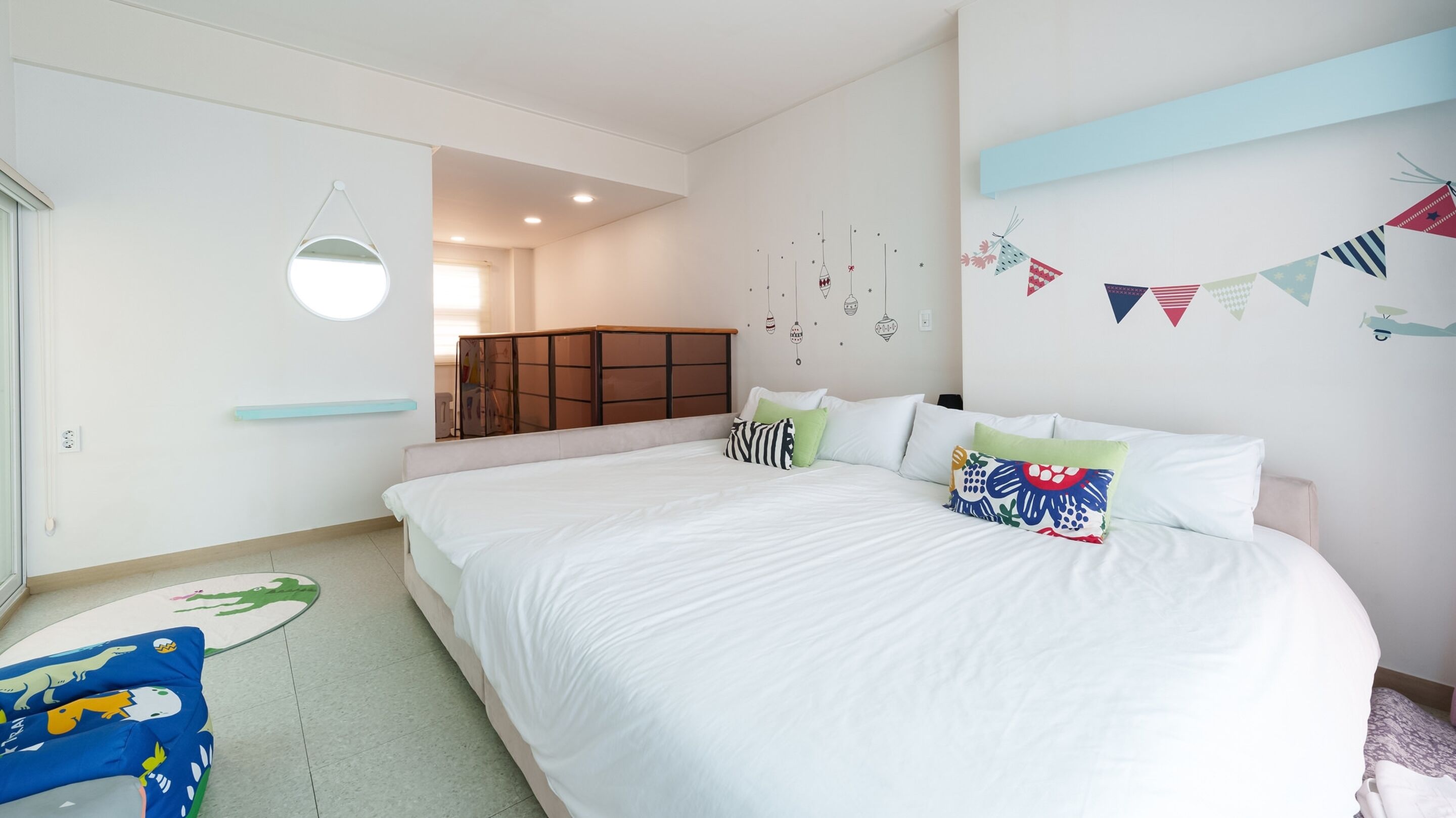A bedroom with a large bed, a wardrobe, a mirror, and a wall with hanging decorations.