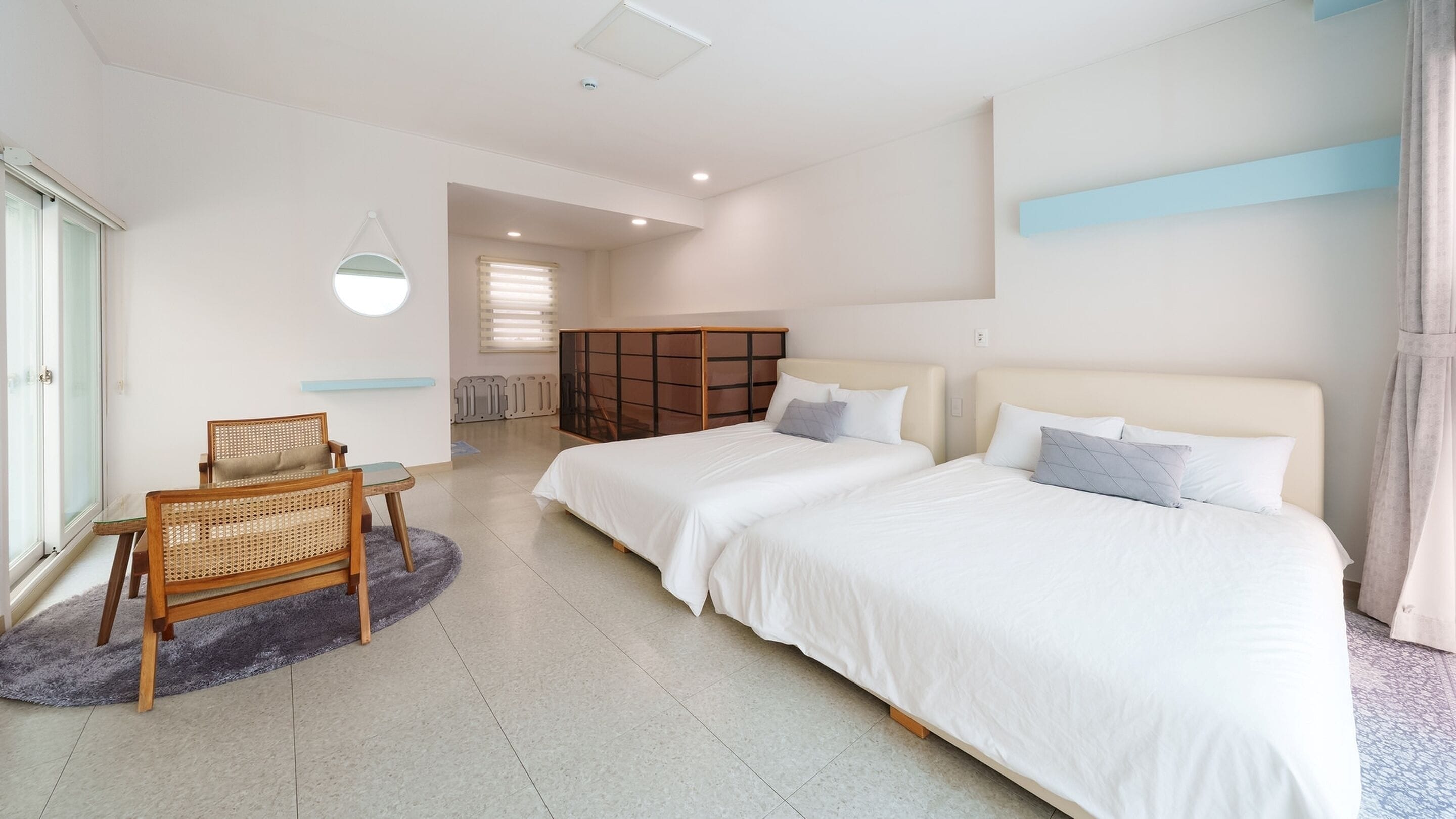 Une chambre d’hôtel moderne avec deux lits, un coin salon comprenant un fauteuil, une petite table et une grande fenêtre.