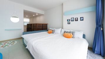 A bedroom with a large bed, two orange pillows, a blue headboard, a small table, and a wardrobe.