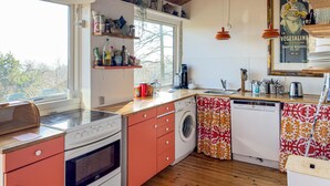 Une cuisine compacte équipée d’une cuisinière, d’un four, d’un lave-linge et d’une fenêtre laissant entrer la lumière naturelle.