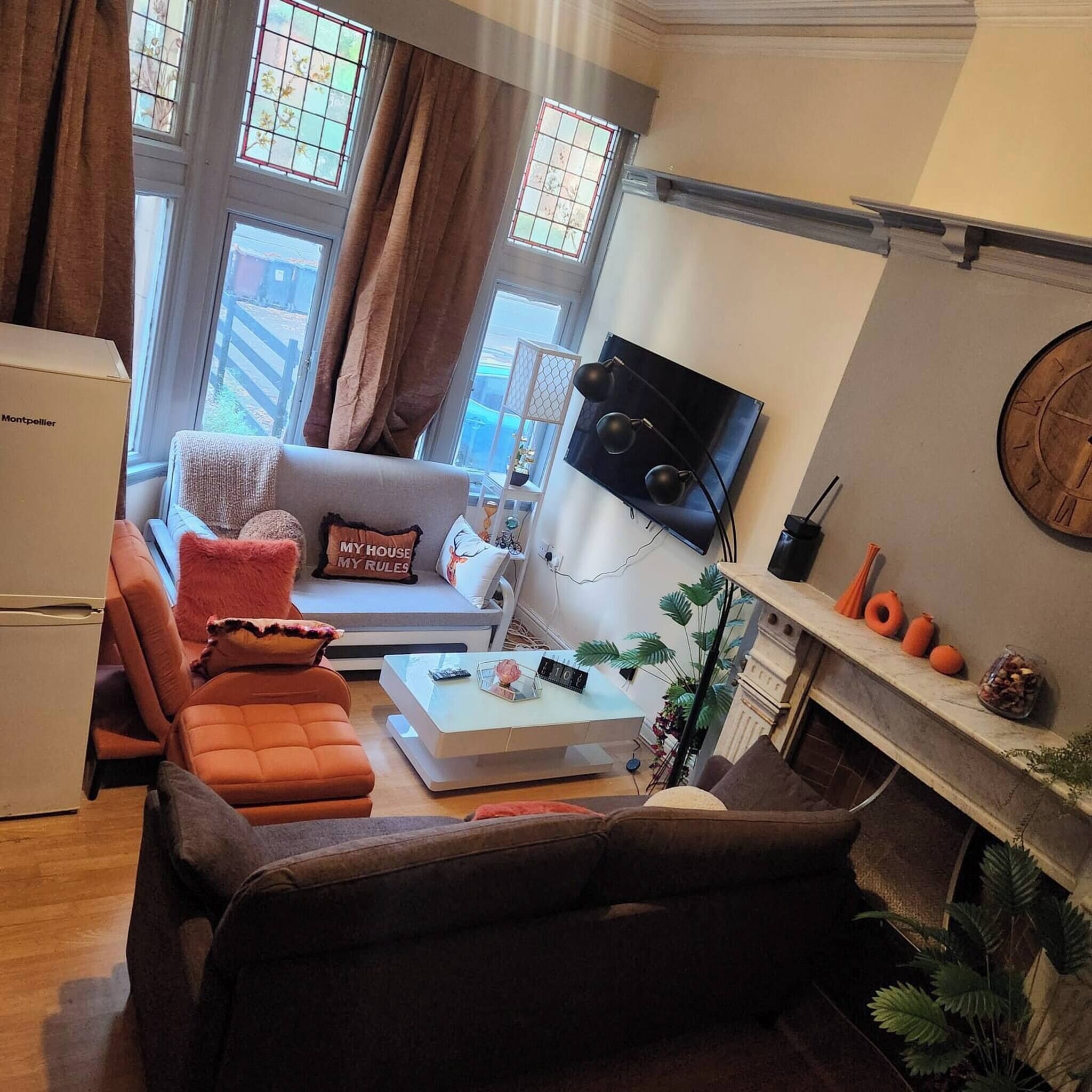 Een woonkamer met een bank, een salontafel, een aan de muur bevestigde televisie en een open haard met decoratieve objecten.