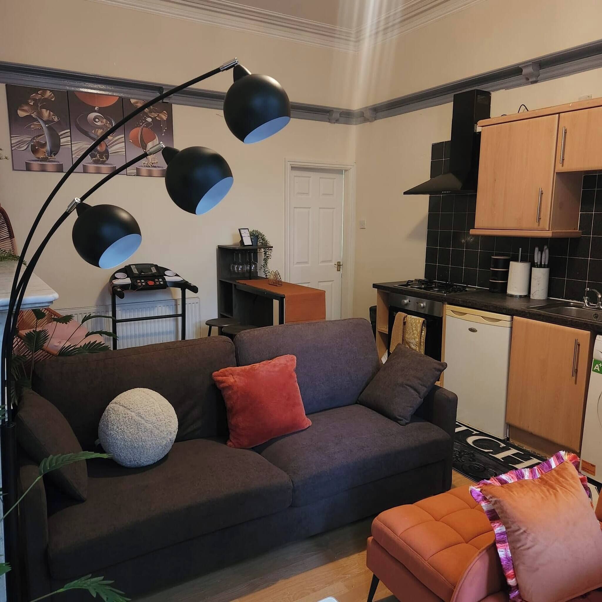 Un espacio habitable compacto con sofá, una pequeña silla naranja, kitchenette y una mesa de comedor.