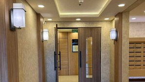 Un corridoio d'albergo con pavimento in piastrelle lucide, pannelli in legno e illuminazione a incasso.