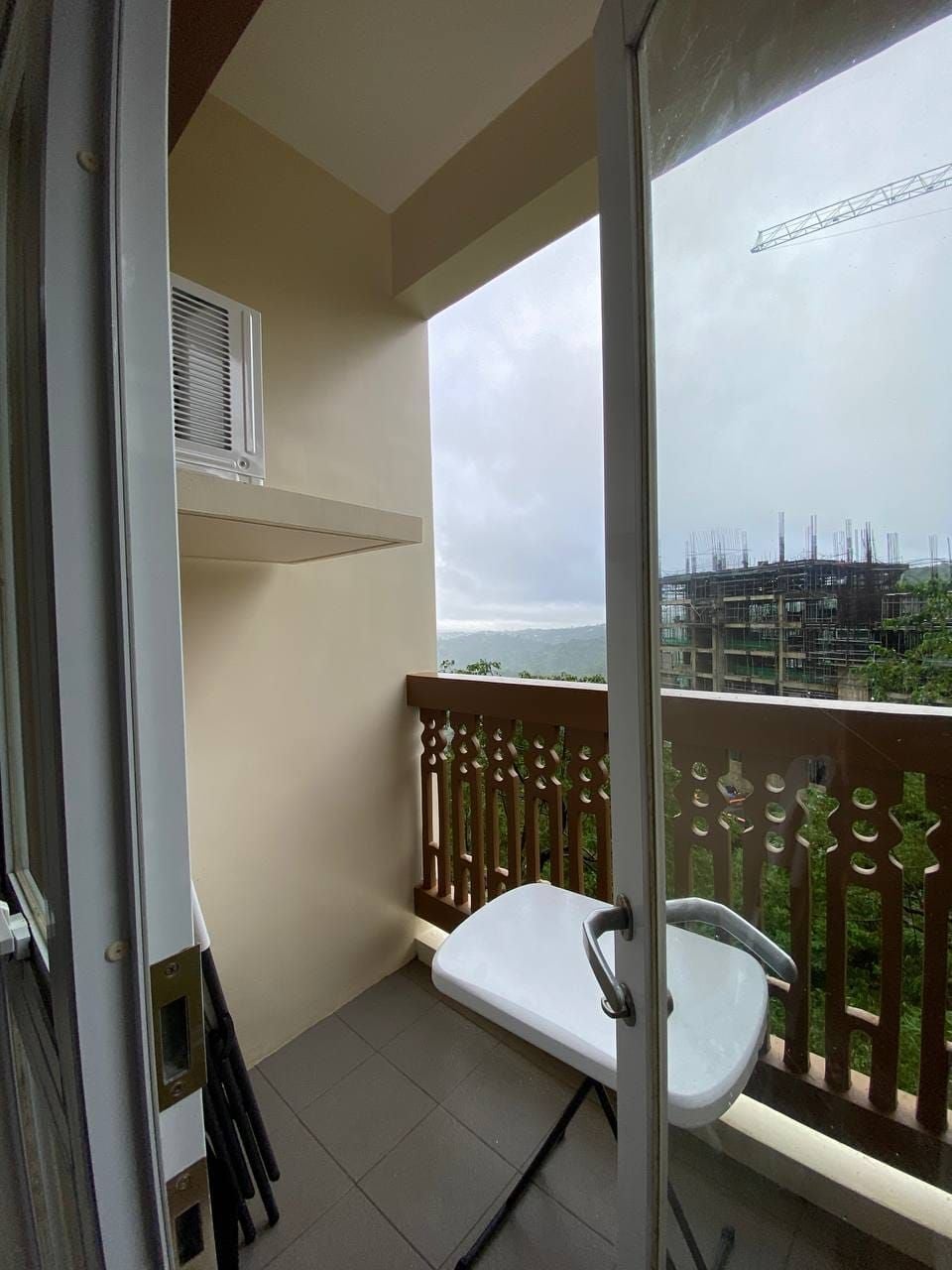 En balkon med en hvid stol, et vindue med udsigt til et byggepladsområde og et metalgelænder.