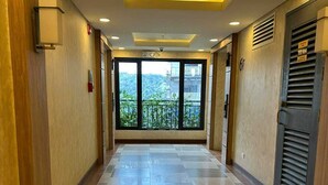 Corridoio di un hotel con pavimento piastrellato, illuminazione a incasso e un'ampia finestra vista su del verde.