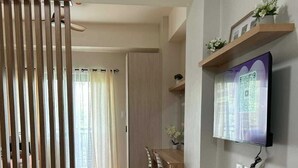 Un soggiorno moderno con pavimento in legno, un divano, un'area pranzo con sedie, una TV a parete e un tavolino con oggetti decorativi.