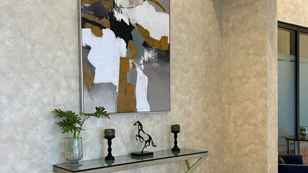 Un interno moderno con un tavolino consolle in vetro, un'opera d'arte astratta e una pianta in vaso.