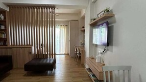 Un soggiorno moderno con pavimento in legno, un divano nero, un tavolo bianco e una TV montata a parete.