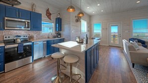 A modern kitchen with blue cabinets, stainless steel appliances, and a central island with stools. - Sleeps 20 • 2 Homes, Beach Boardwalk Access, Private Pools, Stunning Views (Port Aransas)