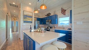A modern kitchen with blue cabinets, a large island with stools, and decorative fish wall art. - Sleeps 20 • 2 Homes, Beach Boardwalk Access, Private Pools, Stunning Views (Port Aransas)