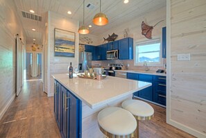 A modern kitchen with blue cabinets, a large island with stools, and decorative fish wall art. - Sleeps 20 • 2 Homes, Beach Boardwalk Access, Private Pools, Stunning Views (Port Aransas)