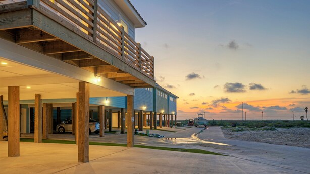A modern building with a covered outdoor area, wooden deck, and a view of the sunset. - Sleeps 20 • 2 Homes, Beach Boardwalk Access, Private Pools, Stunning Views (Port Aransas)