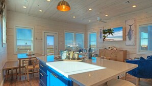 A spacious kitchen with a large island, wooden cabinets, and a dining area with a bench and chairs. - Sleeps 20 • 2 Homes, Beach Boardwalk Access, Private Pools, Stunning Views (Port Aransas)