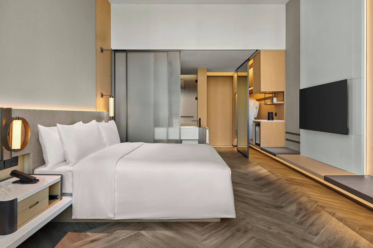 A modern hotel room with a large bed, bedside table, and a flat-screen TV mounted on the wall.