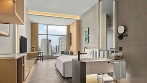 Une chambre d’hôtel moderne dotée d’un grand lit, d’un bureau, d’une salle de bain avec un grand miroir et offrant une vue sur la ville.