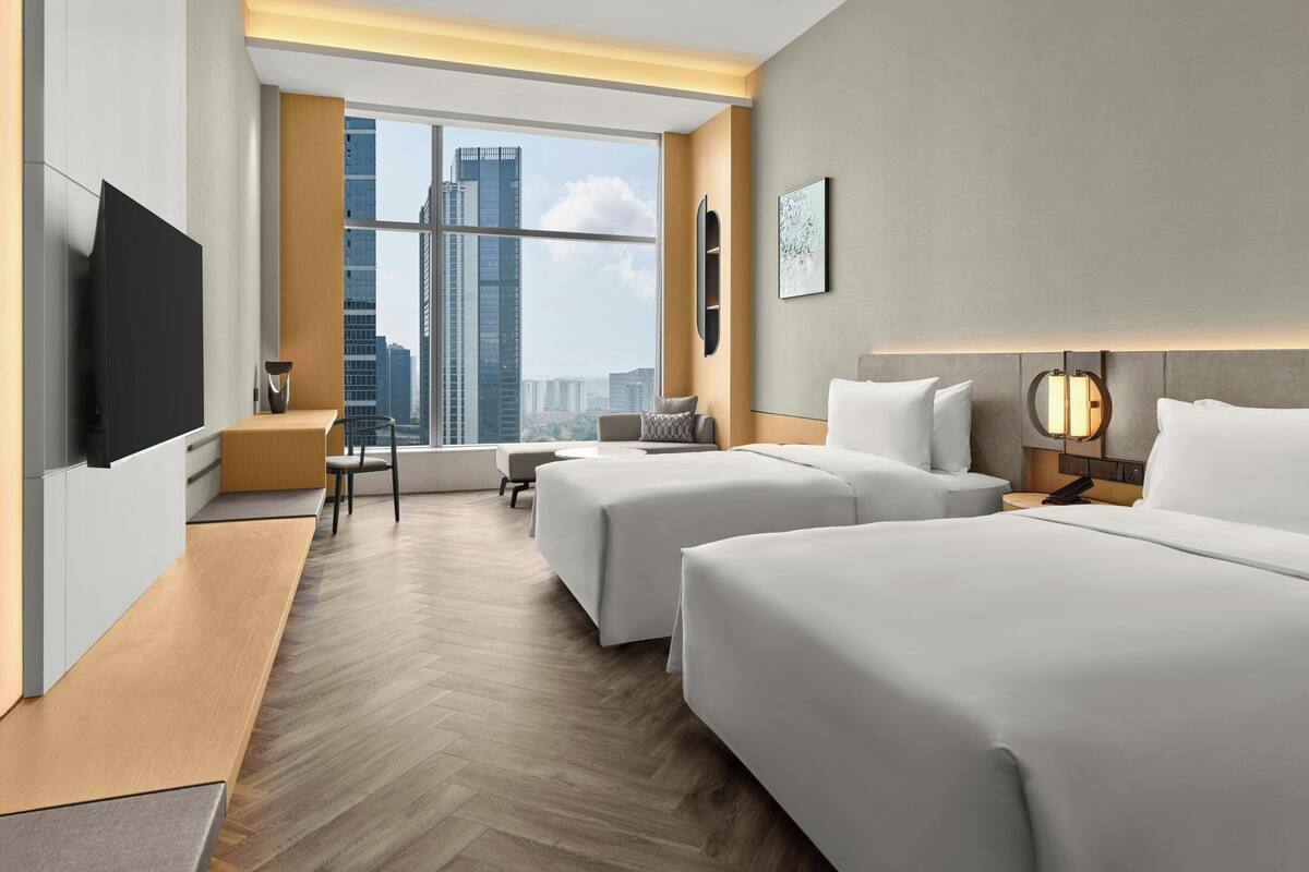 A hotel room with two beds, a TV, a desk, and a view of tall buildings.