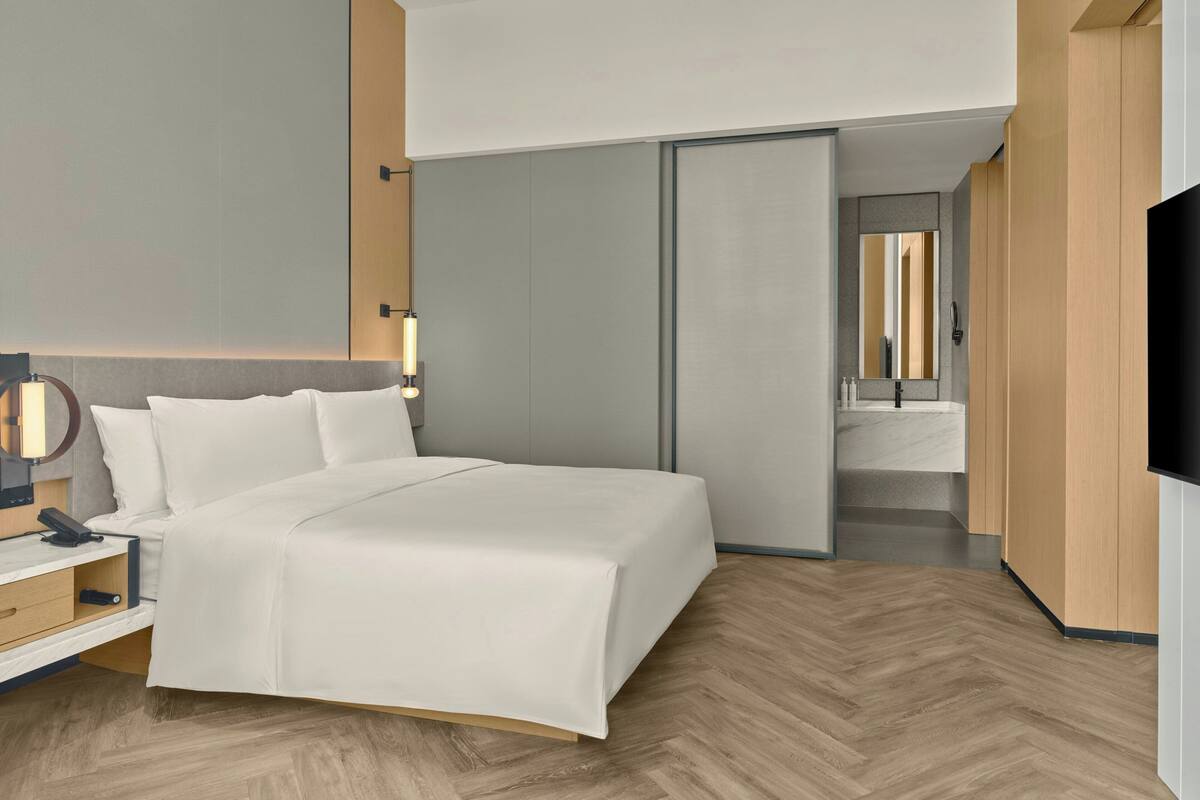 A modern hotel room with a bed, bedside table, lamp, and a TV.