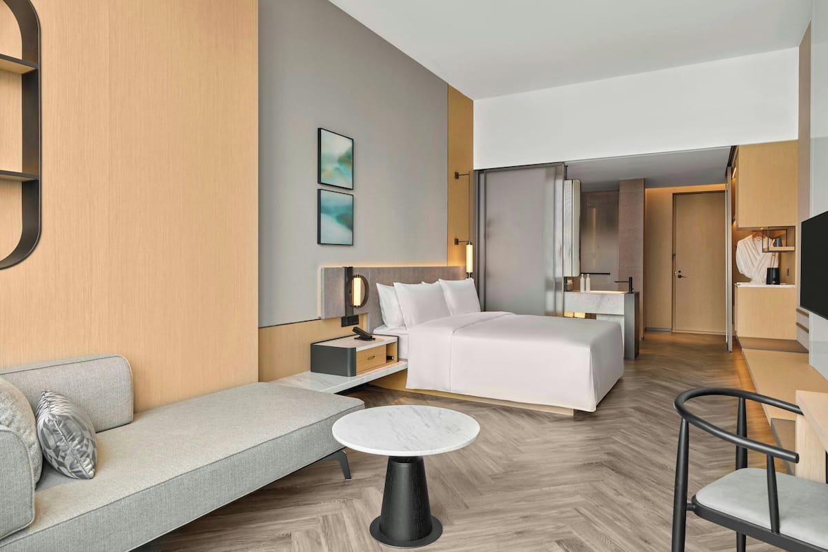 A modern hotel room with a bed, sofa, bedside table, lamp, and a small round table.