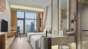 Une chambre d’hôtel moderne dotée d’une grande fenêtre, d’un téléviseur à écran plat, d’un canapé-lit, d’une coiffeuse avec miroir et d’une petite table.