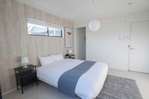 A bedroom with a bed, a nightstand, a lamp, a picture frame, a door, and a light fixture. - 4BR Modern Home Near Kumamoto Airport by Restavio (Ozu)