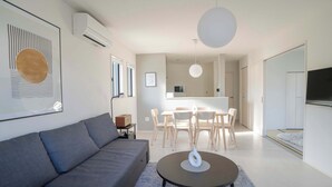 Ein modernes Wohnzimmer mit Sofa, Esstisch mit Stühlen, Küchenzeile und Fernseher.