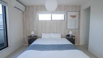 A modern bedroom with a large bed, two bedside tables with lamps, a window, and an air conditioning unit.