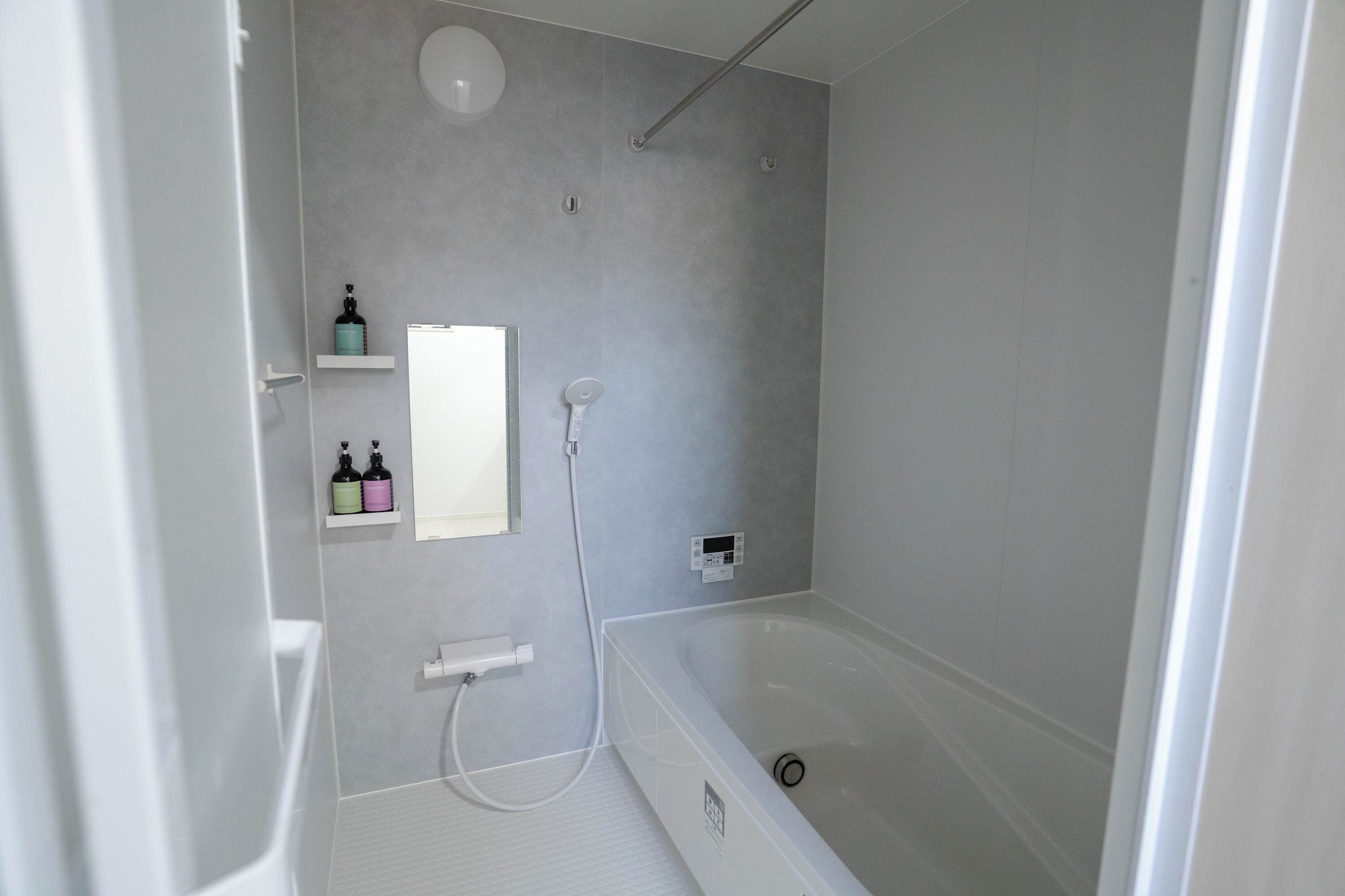 Un baño moderno con bañera, ducha y inodoro. Hay estantes con artículos de aseo y un espejo.